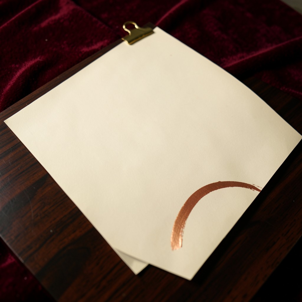 One large cream sheet with a single copper arc, held by a brass clip on dark wood